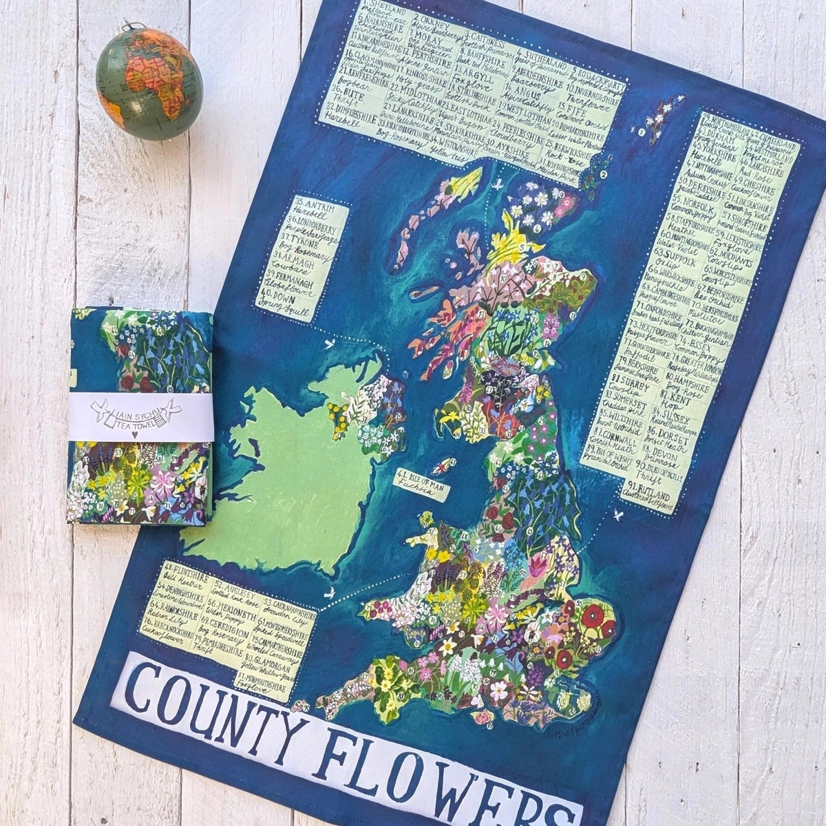 Tea towel featuring a map of England with floral county flowers design on a wooden surface