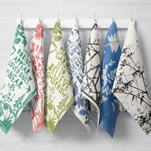 Set of colorful tea towels with various patterns hanging on a rack.