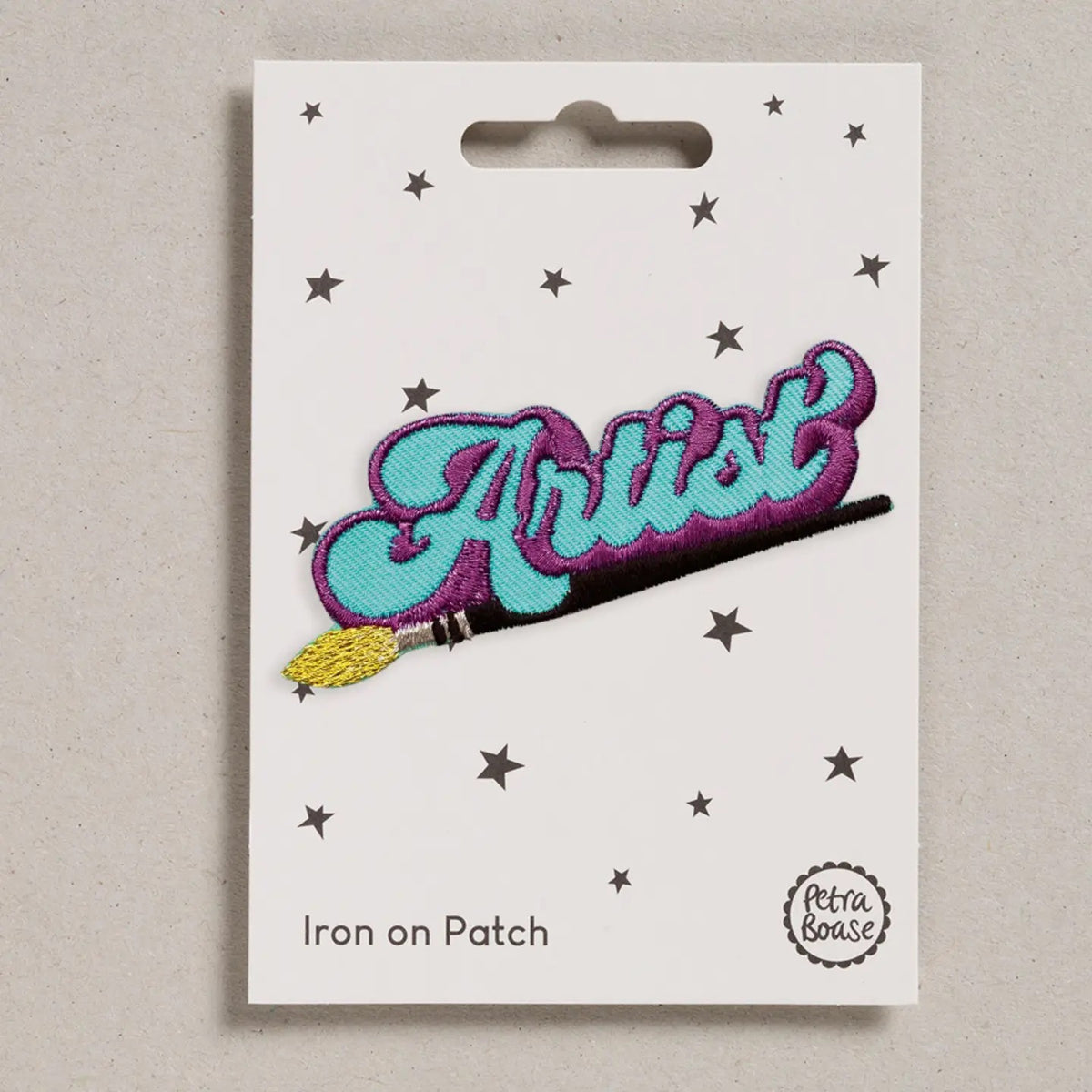 Iron on patch with 'Artist' and paintbrush design on a white card with star patterns.