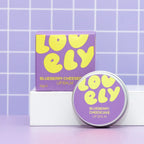 Blueberry Cheesecake flavoured lip balm in a round metal next to it's box on a purple background