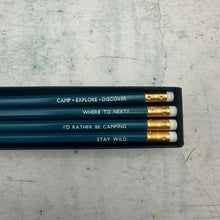 Four teal coloures pencils in a black gift box. The pencils have white erasers with gold metal ferrules and printed white text reading 'CAMP • EXPLORE • DISCOVER', 'WHERE TO NEXT?', 'I'D RATHER BE CAMPING', and 'STAY WILD'.
