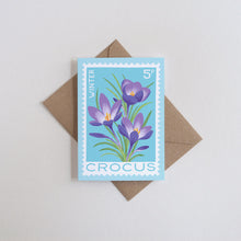 Rectangular mini card featuring a light blue background with an illustration of purple crocuses and green leaves, placed on top of a brown envelope against a light gray background.