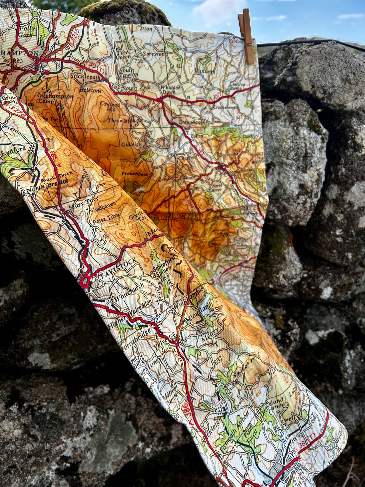Close up of Dartmoor map tea towel shown against a stone wall.