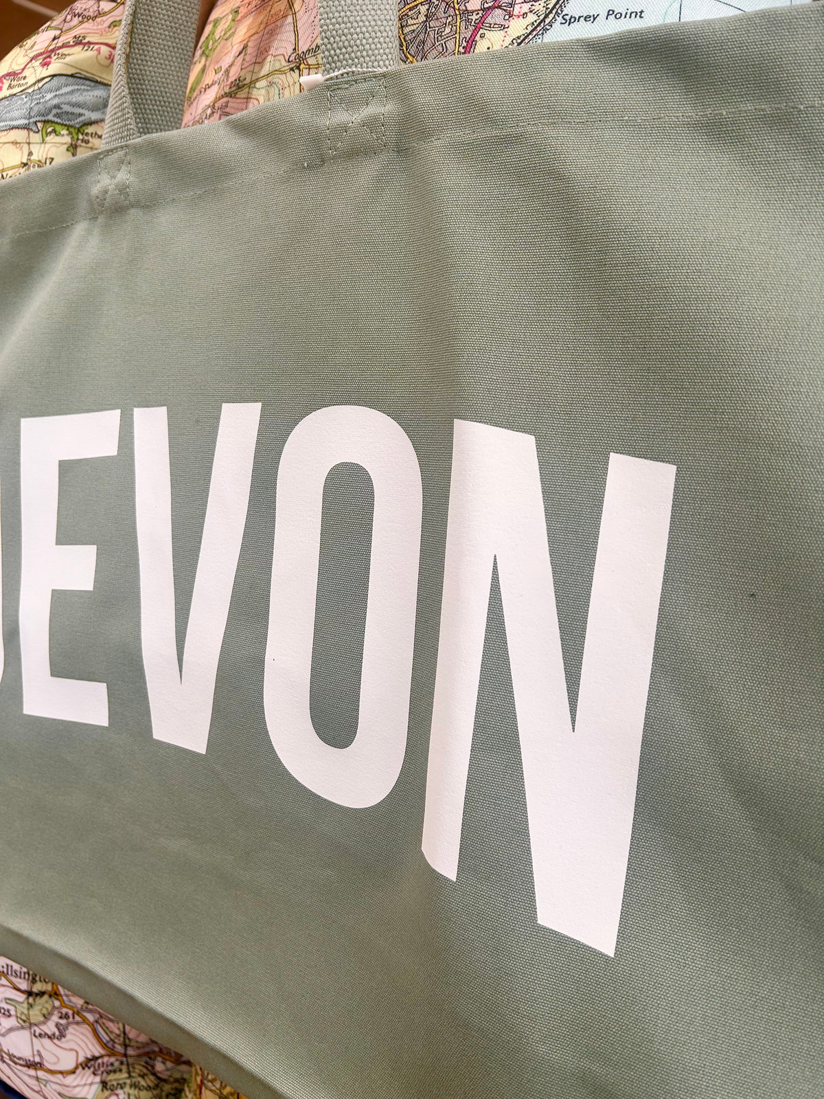 Close up of green bag with 'DEVON' printed on it, against a patterned background