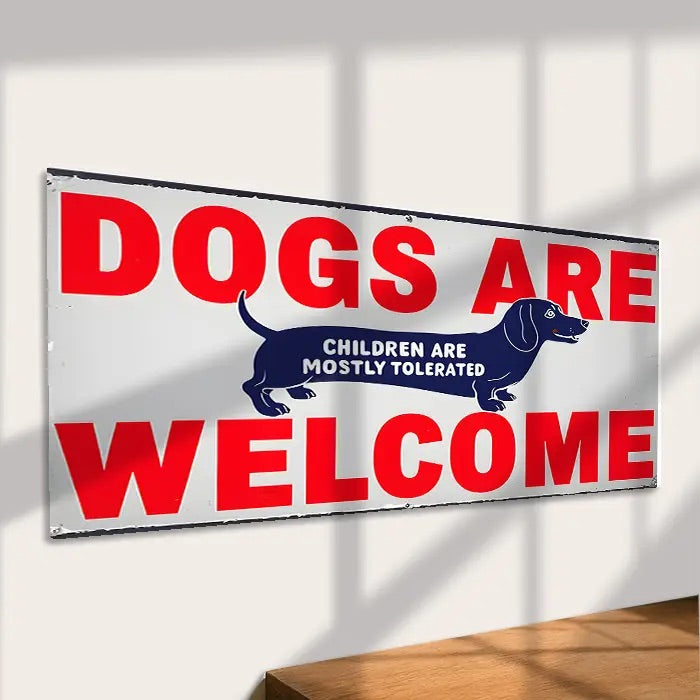Sign with 'DOGS ARE WELCOME' text and dachshund illustrations on a white wall.
