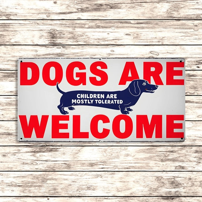 Metal sign with dachshund dog and red text 'Dogs are welcome, children are mostly tolerated' on a wooden background
