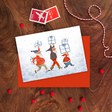 Greeting card with elves carrying gift boxes on a wooden surface with decorative elements.
