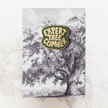 Pin with 'Expert Tree Climber' text in gold on a green background, shown on a backing card with illustration of large tree