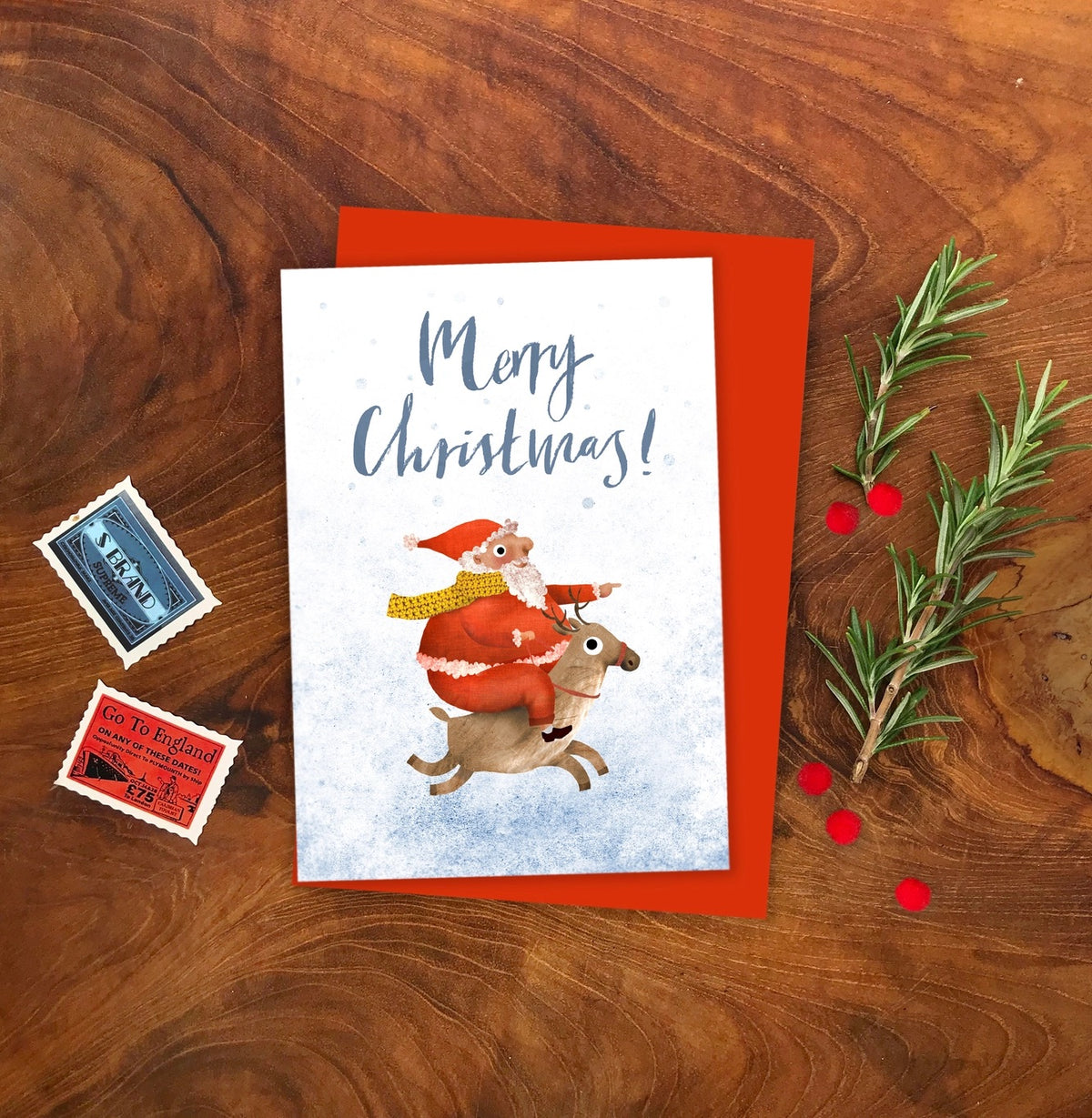 Christmas card with Santa Claus and reindeer on a wooden surface with decorative elements.