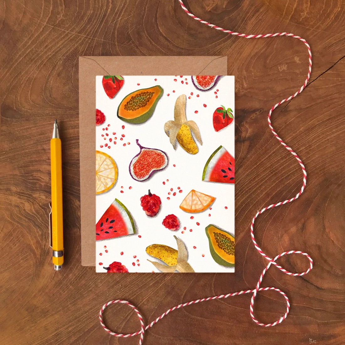 Greeting card with fruit pattern on a wooden surface with a pen and string.