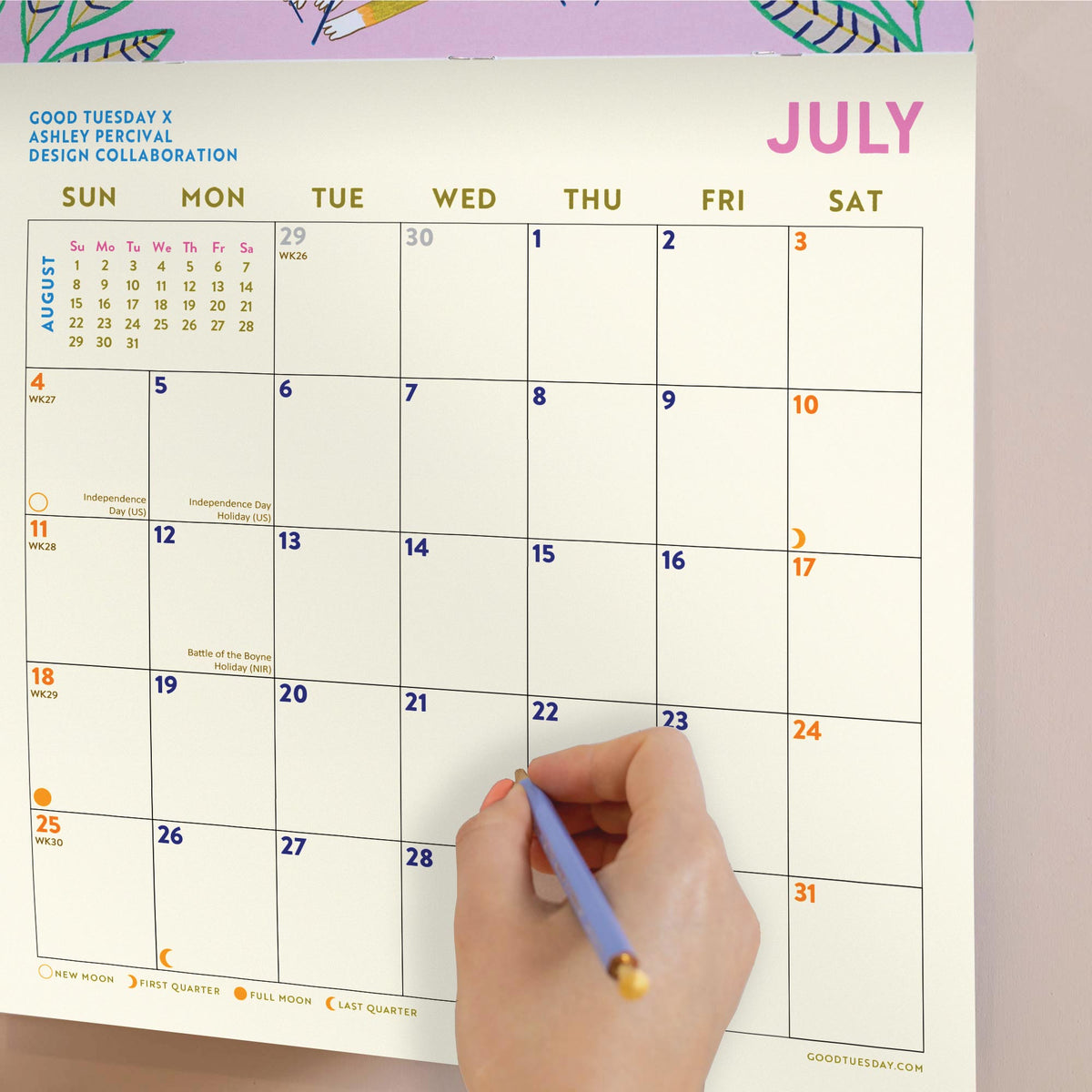 Hand holding a pen writing on a July page of a calendar