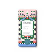 A single rectangular chocolate bar wrapped in a colorful geometric paper sleeve, centered on a plain white background. The wrapper features a pink top section, a blue bottom section, and a central white panel with black text reading 'COCO GINGERBREAD MILK CHOCOLATE'.