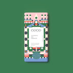 A rectangular milk chocolate bar with a colorful geometric pattern wrapper, centered on a solid green background. The wrapper features a white center label with the brand name 'COCO' and the text 'GINGERBREAD MILK CHOCOLATE'.