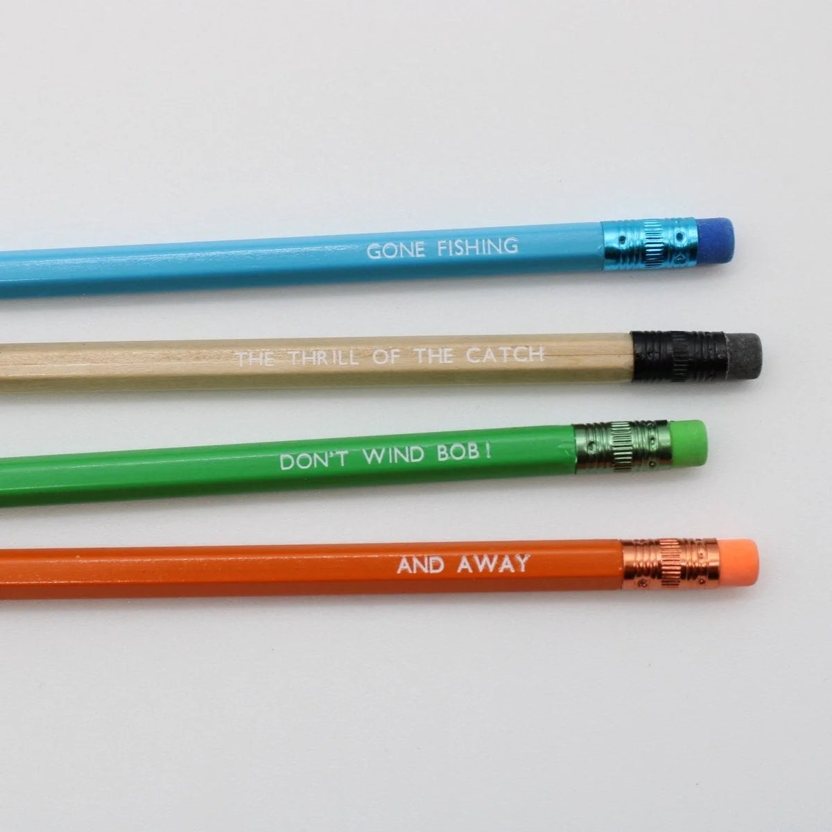 Four wooden fishing-themed pencils arranged on a plain white background. The pencils are blue, natural wood, green, and orange, each printed with a phrase from the TV show Gone Fishing.