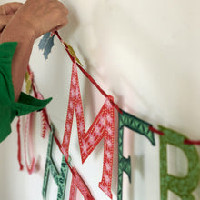Person hanging Merry Christmas banner with letters on a white wall