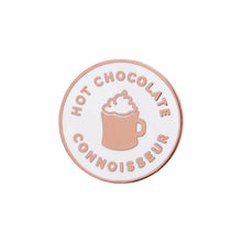 Round enamel pin with 'Hot Chocolate Connoisseur' text and a mug illustration on a white background.