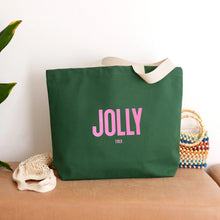 Dark green tote bag with pink text 'JOLLY' in large font and 'tired' in a much smaller font underneath.
