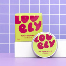 Lovely Skincare's Juicy Pineapple Lip Balm shown with its box and round tin container, set against a purple tiled background.