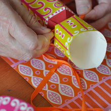 Close-up of hands tying a bright orange ribbon around the end of one of their freshly made crackers.