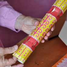 A person's hands holding a colourful paper cracker, which is decorated with yellow, pink and red patterns.