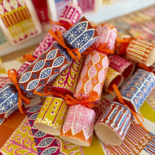 A pile of colourful patterned paper Christmas crackers tied with orange ribbons, arranged on a surface filled with beautiful Cambridge Imprint papers.
