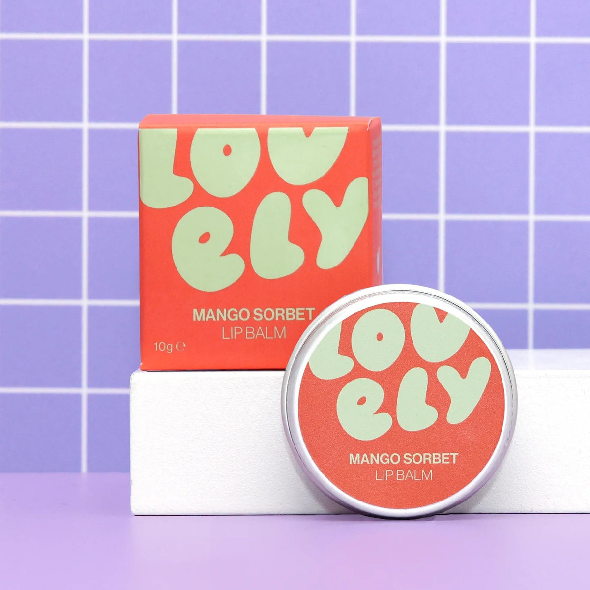 Lovely Skincare's mango sorbet lip balm with packaging on a purple grid background