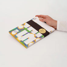 A hand holding a Meal Plan notepad with a sunflower background, set against a plain white background.