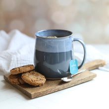 Blue mug with a tea bag on a wooden tray with cookies and a spoon.