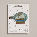 Iron on patch of a ship in a bottle with 'Mothership' text on a white card, brand 'Petra Boase' visible.