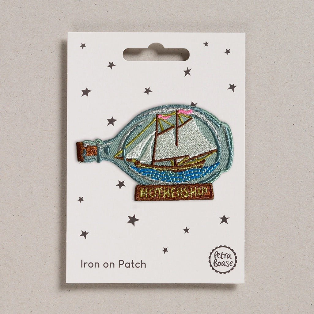 Iron on patch of a ship in a bottle with 'Mothership' text on a white card, brand 'Petra Boase' visible.