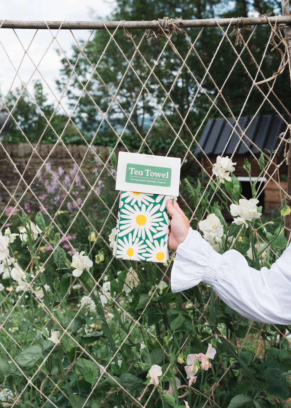 Person holding a green tea towel with daisy design against a garden fence.