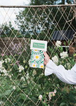Person holding a green tea towel with daisy design against a garden fence.