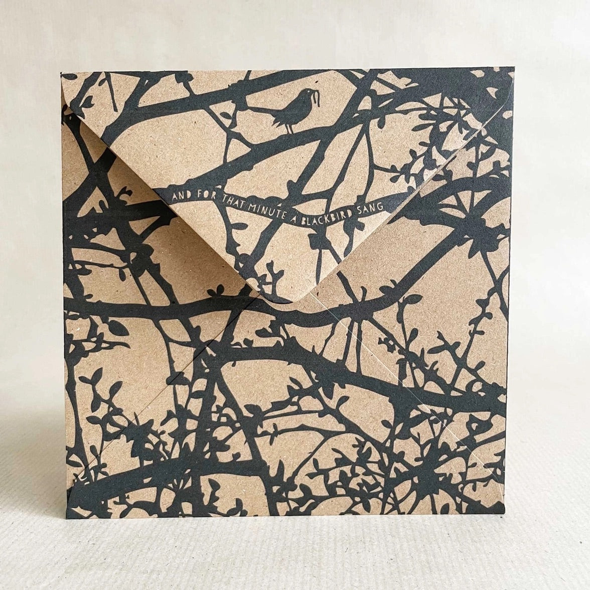 Printed kraft envelope back with black tree branch and bird design on a beige background