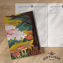 Front cover of reading logbook with mushroom and forest design plus an open logbook showing the inside pages against a wooden tabletop background. 