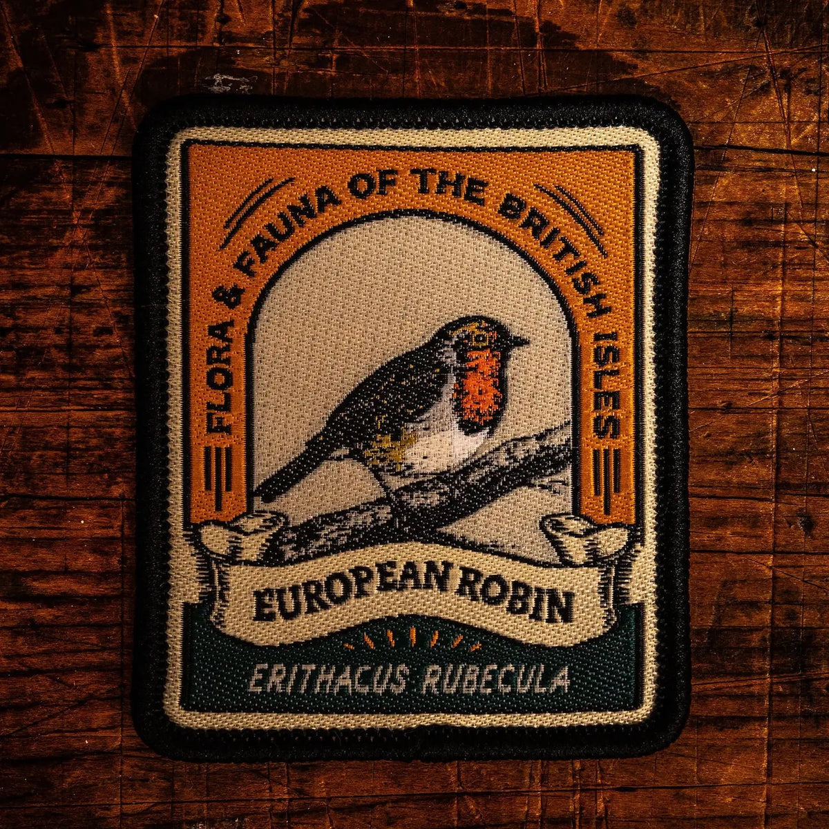 An embroidered patch featuring a European robin bird perched on a branch, with the text 'FLORA & FAUNA OF THE BRITISH ISLES', 'EUROPEAN ROBIN', and 'ERITHACUS RUBECULA' on a rustic dark wood background.