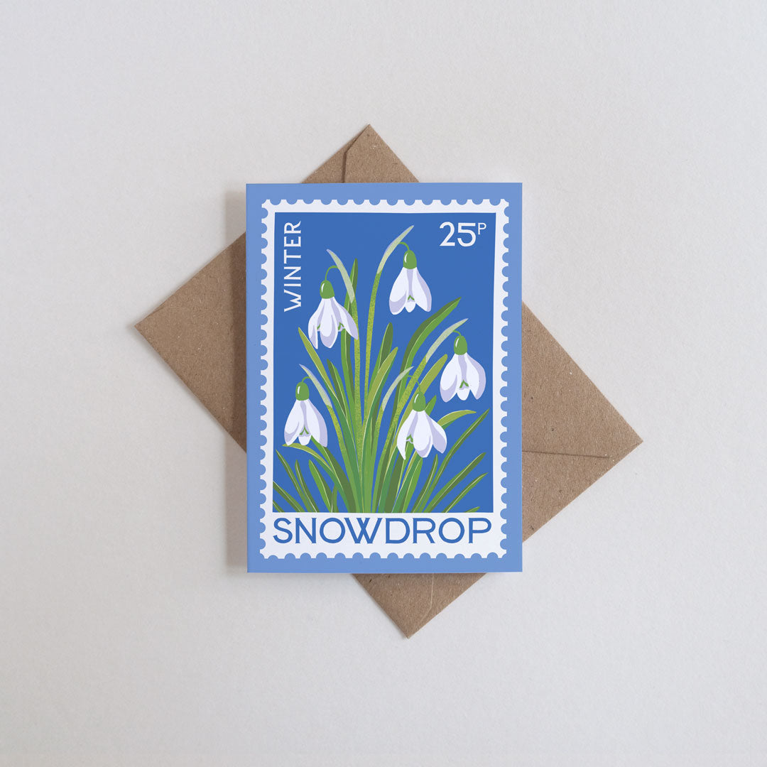 Mini card with snowdrop stamp design on a blue background with stamp edging. Shown on a brown kraft envelope.