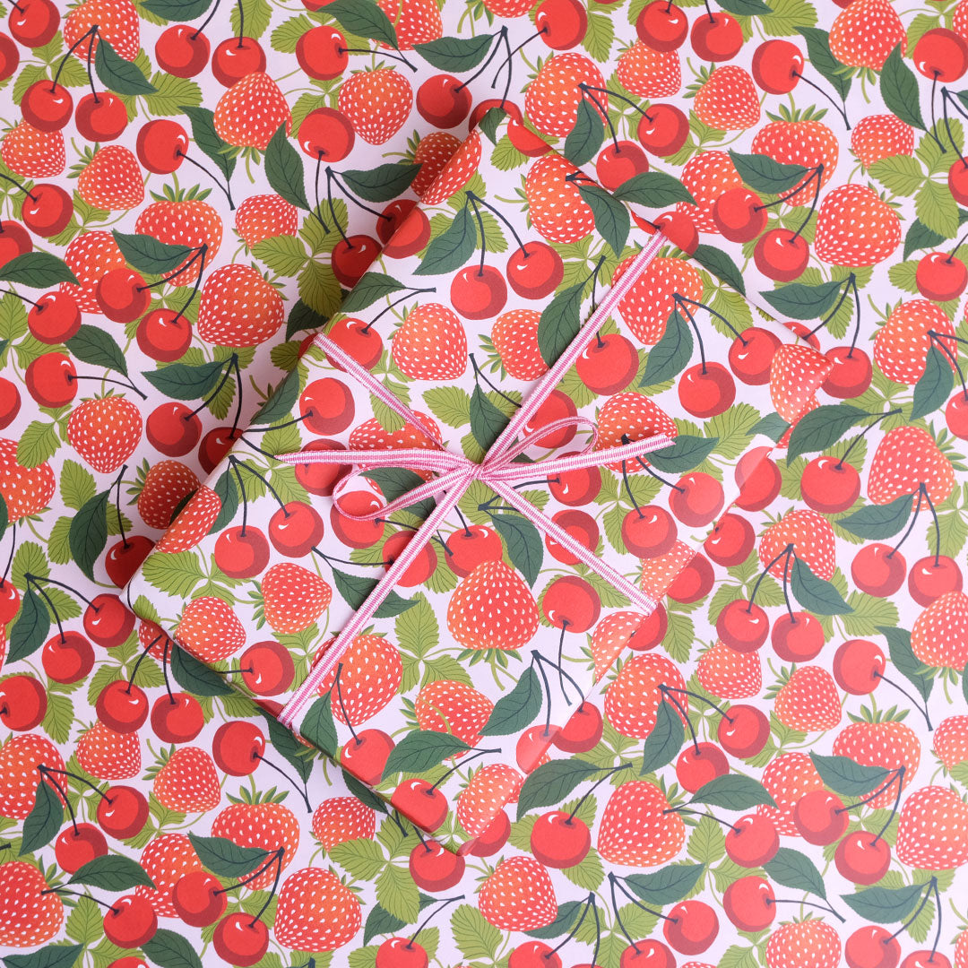 Present wrapped in strawberry and cherry print paper with bow on a background of the same paper. 