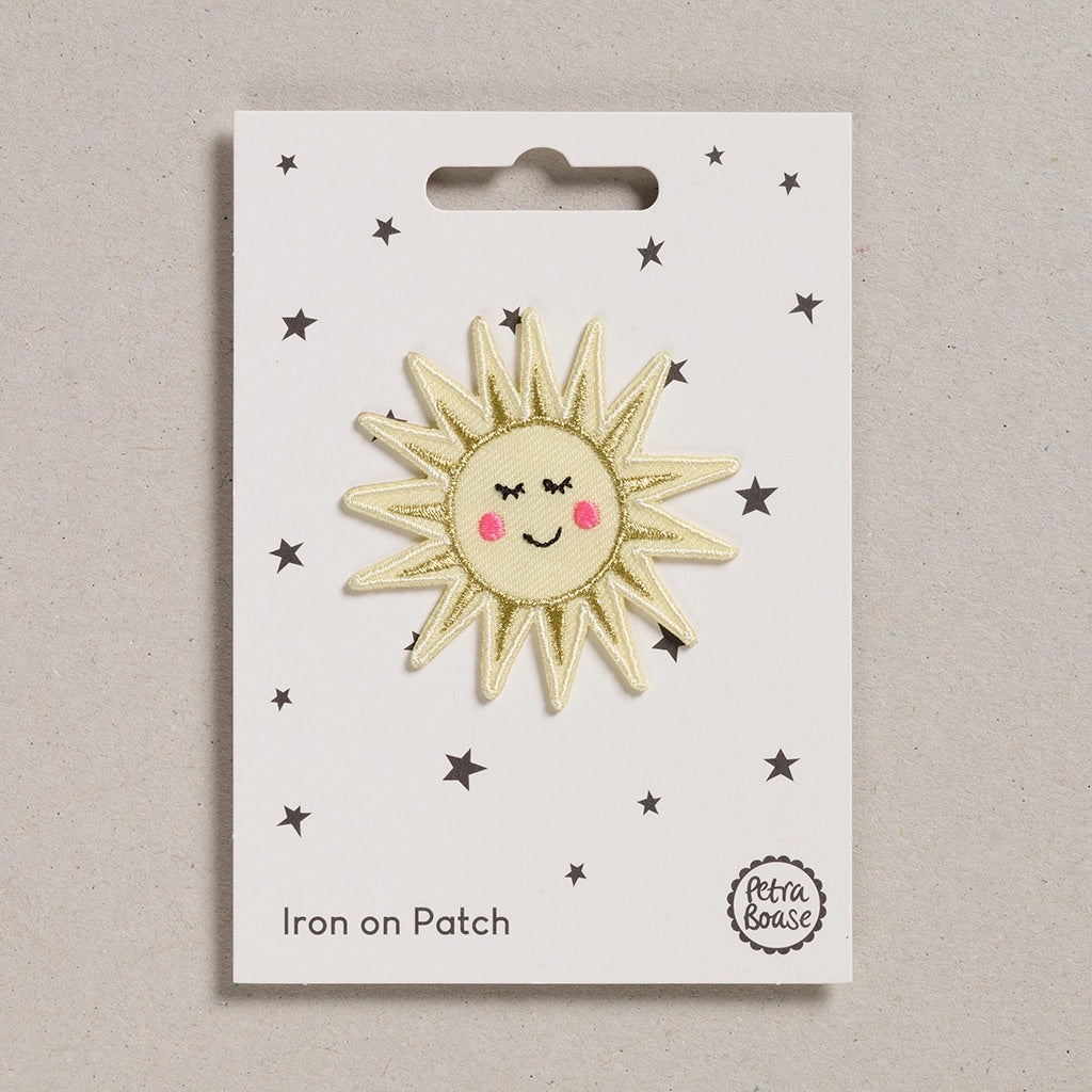 Sun-shaped iron on patch with a smiley face on a white card with star designs, branded 'Petra Boase'.