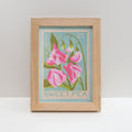 A framed art print featuring a vintage-style sweet pea stamp illustration with pink flowers on a light blue background, set in a light oak wood frame against a neutral white background.