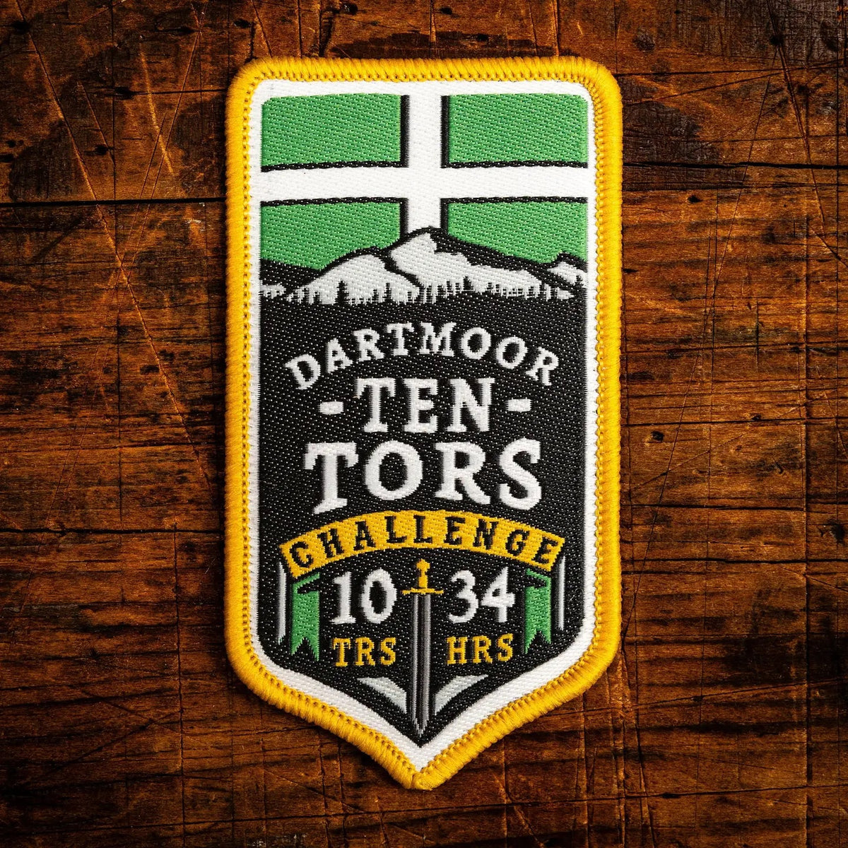 Dartmoor Ten Tors Challenge embroidered patch against a wood background.