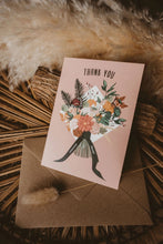 A pink thank you card with a floral bouquet illustration and the words 'THANK YOU' at the top and 'sooooooo much!' on the ribbon tails, placed on a brown envelope.