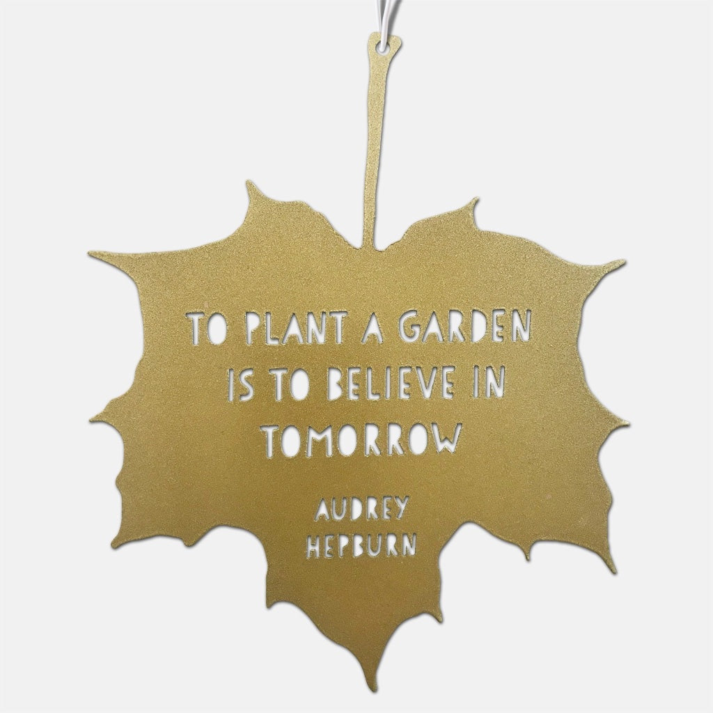 Gold leaf-shaped sign with a quote by Audrey Hepburn on a white background