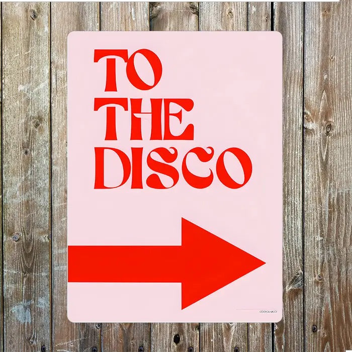 Pink sign with red text 'TO THE DISCO' and a red arrow on a wooden background