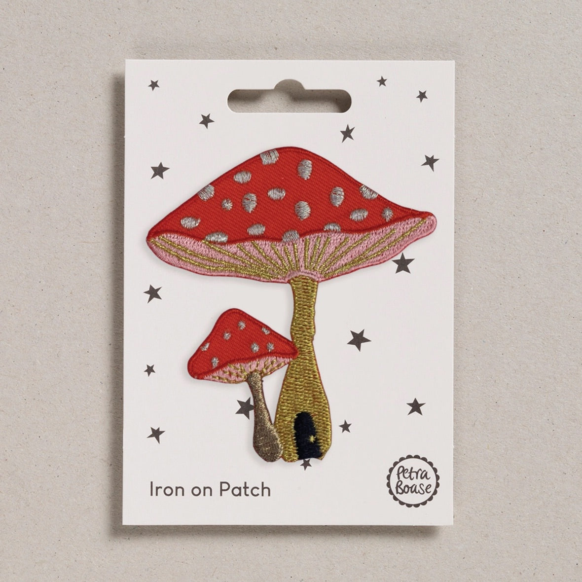 Iron on patch of red toadstools with gold stems on a white card with star patterns, branded 'Petra Boase'.