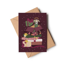 A Christmas card featuring an illustration of a dog peeking out of a stack of wrapped Christmas presents on a dark burgundy background with white stars. A brown kraft envelope behind it.