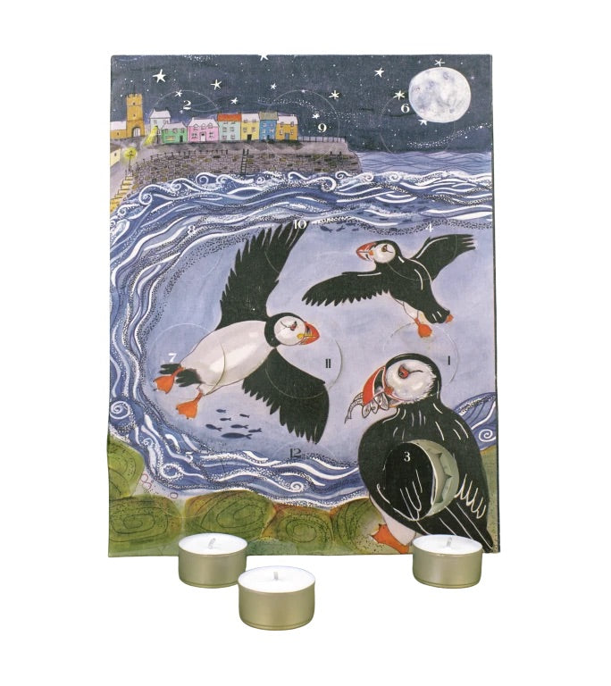 Advent calendar featuring a painted puffin scene at night, with three small tealight candles placed in front on a white background.